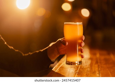 close-up on a wooden bar table guy holds a glass of light beer warm lighting light - Powered by Shutterstock