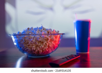 Close-up. On a wooden table are a glass bowl of popcorn, a carbonated drink in a plastic glass, and a TV remote control. Home comfort, watching your favorite movies, TV shows, relaxing. - Shutterstock ID 2169314135