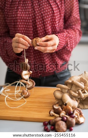 Closeup on young housewife stringing mushrooms on string