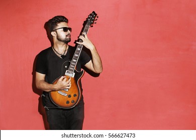 Closeup of one handsome passionate expressive cool young brunette rock musician men playing electric guitar standing against red background