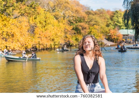 Closeup of one happy young woman in Central Park in New York City nyc by The Lake during sunny autumn day with people rowing on romantic boats, gondolas in water