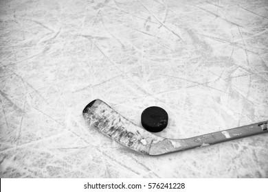 Closeup of one hockey stick and puck laying on textured ice in black and white