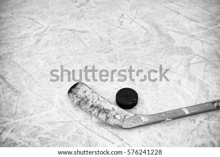Closeup of one hockey stick and puck laying on textured ice in black and white