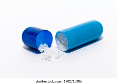 Close-up one opened blue soft capsule pill with white powder on white background. medicine supplement vitamin