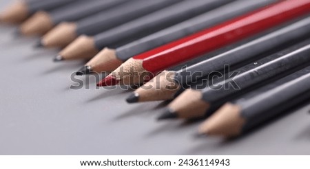 Closeup of one red wooden pencil among many black background. Distinctive personality traits concept