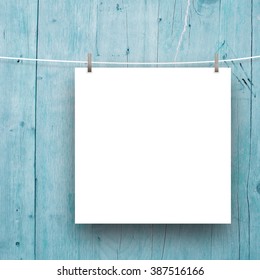 Close-up of one square paper sheet frame with pegs on aqua wooden boards background