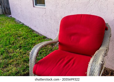 Closeup Of One Wicker Outdoor Armchair Chair Outside With Red Cushion At Front Yard Or Backyard With Green Grass Lawn At Sunset In Naples, Florida