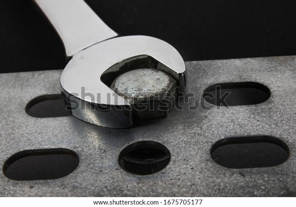 closeup of an open end wrench on a bolt head\
on a black background