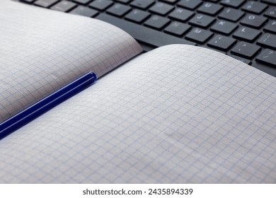 Close-up of an open graph notebook with blue pen on laptop keyboard