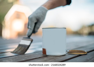 Close-up, an open jar and a man's hand in a work glove with a painting brush paints boards outdoors. A hand applies paint, oil or varnish to the veranda floorboards - Powered by Shutterstock