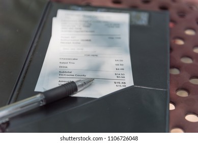 Close-up Open Leather Bill Holder With Restaurant Check And Pen. Top View, Soft Focus Receipt With Total Amount On Outdoor Picnic Table, Natural Light. Customer Payment For Cafe Service