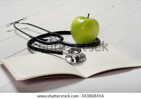 Closeup open notebook with blank pages with stethoscope and apple on a white doctor's table. Free space for text. Copy space. Top view