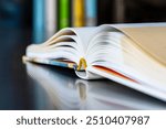 Close-up opened book with reflection on metal desk, library bookshelf in toned background