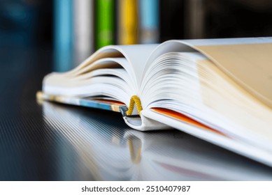 Close-up opened book with reflection on metal desk, library bookshelf in toned background