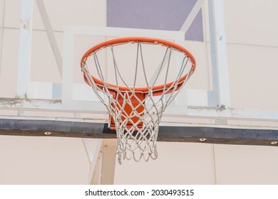 Closeup of orange basketball hoop with rope net against glass backboard.