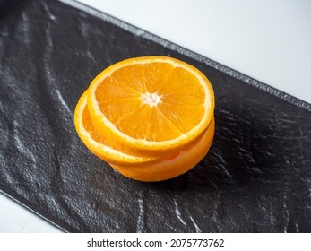 A close-up of an orange cut into slices lies on a dark textured plate. Delicious beautiful fruit full of vitamins. Top view, flat lay