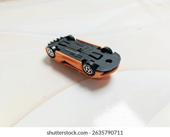 Close-up of orange die-cast model car with black side trim and white-rimmed wheels. Toy vehicle for kids or collectors.