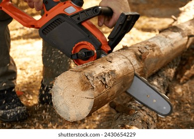 Closeup of an orange electric chainsaw cutting through a thick log of wood 