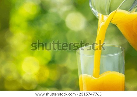 closeup of orange juice pouring into glass from jug on green blurred background Imagine de stoc © 