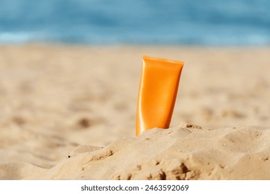 close-up of an orange sunscreen bottle placed on a sandy beach with the sea in the background - Powered by Shutterstock