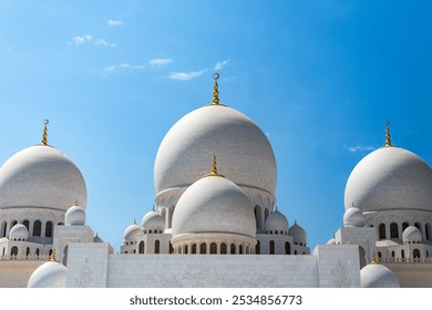 Close-up of the ornate domes of Sheikh Zayed Grand Mosque, focusing on the gold details and smooth white surfaces against the clear blue sky. - Powered by Shutterstock