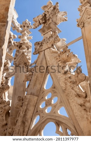 Close-up of ornate gothic marble stone carvings and intricate tracery architectural details against a bright blue sky at the Milan Cathedral.