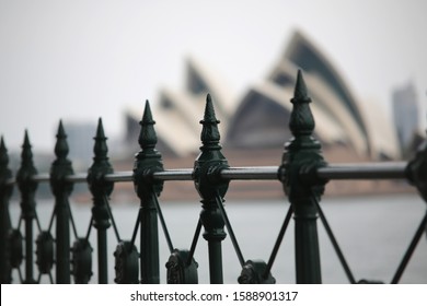 A Close-up Of An Ornate Green Fence With A Blurry Sydney Opera House In The Background 