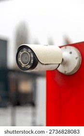 Close-up of outdoor CCTV security camera mounted on red wall. Surveillance system in urban environment.