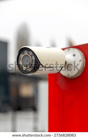 Close-up of outdoor CCTV security camera mounted on red wall. Surveillance system in urban environment.