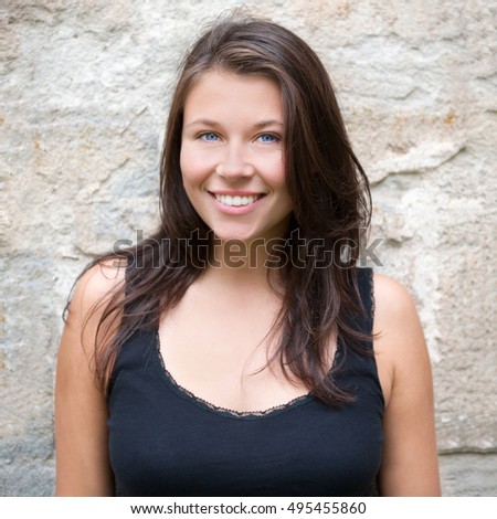 Closeup outdoor portrait of a beautiful smiling girl in black top in front of an old wall