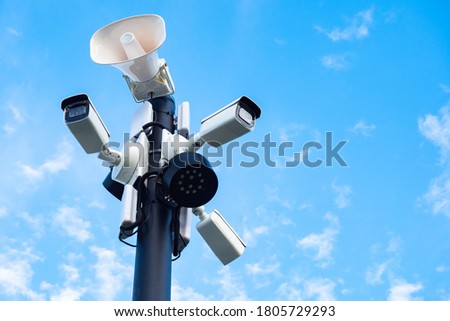Close-up of outdoor surveillance cameras, floodlights and loudspeakers on a street pole. Ensuring security on the street. Security cameras and speakers on a pole above a blue sky.