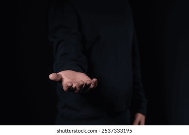 A close-up of an outstretched hand, palm facing upward, in a dark setting. The person is wearing dark clothing. Concept of help, offer, or request - Powered by Shutterstock