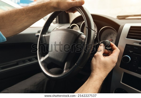 Closeup over the shoulder view of unrecognizable\
man sitting in a car on driver\'s seat, turning on windshield\
wipers. Male driver riding in the city in the rain, holding hands\
on steering wheel