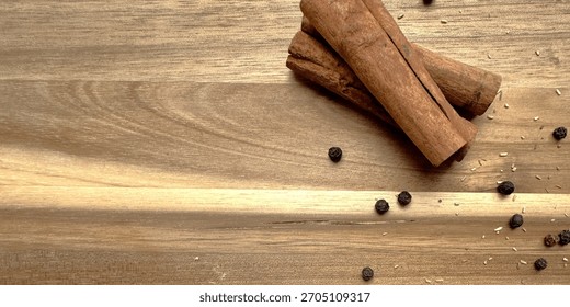 Close-up, overhead view emphasizing the rolled texture of the cinnamon sticks and scattered black peppercorns against a warm, horizontal wooden board, ideal for cooking blogs and holiday recipes.