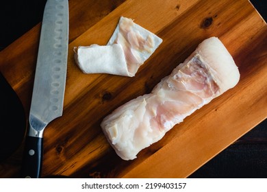 Close-up Overhead View Of A Skinned Halibut Fillet On A Wood Cutting Board: Raw White Fish Fillet With Skin Removed With A Kitchen Knife