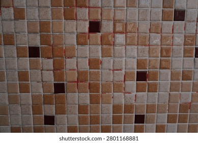 A close-up, overhead view of a tiled surface with alternating light and dark brown square tiles. Some grout lines show red and green discoloration