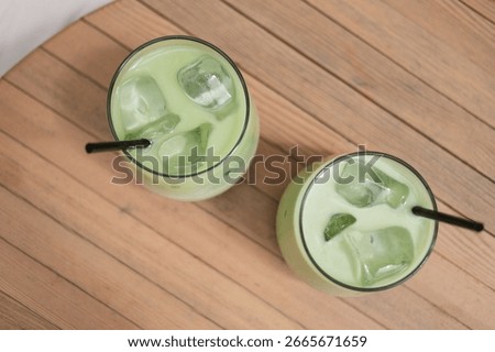 Close-up overhead view of two iced matcha latte drinks on a garden table.