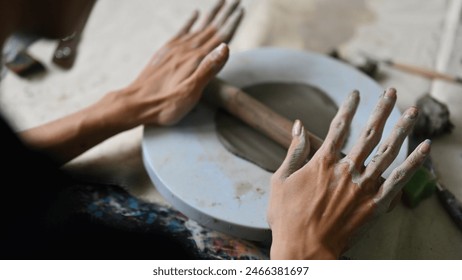 Close-up over-shoulder image of Young potter rolling out clay, Skillful Young artisan at work, rolling clay with a rolling pin. - Powered by Shutterstock