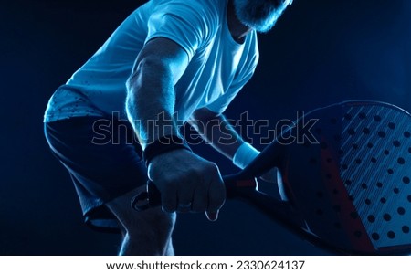 Closeup padel tennis player with racket. Man athlete with paddle tenis racket on court with neon colors. Sport concept. Download a high quality photo for the design of a sports app or betting site.