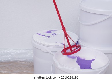 Close-up Of Paint Buckets And A Stirrer, Against A White Wall