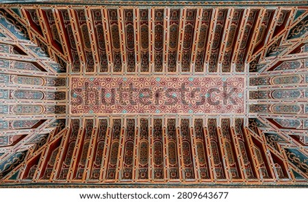 A close-up of the painted cedar ceiling panels of the Mosque Qaddour al-Alami shows the richly decorated coffered wooden structure with geometric star patterns in multicolored paint radiating from a central panel.