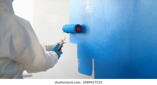 Close-up of painter with brush tool covered in blue colour painting wall. Renovation interior design, construction site and project concept - Powered by Shutterstock