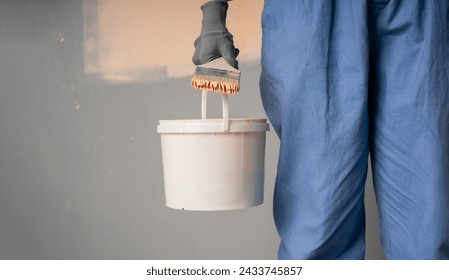 Close-up of a painter with a bucket and brush standing near the wall. Wall painting tool concept. Copy space - Powered by Shutterstock