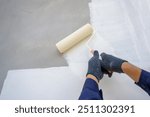 A close-up painter of a recently constructed home, A painter expertly paints a house while gripping a paint roller. A painter primes a building that is still under construction with white paint.