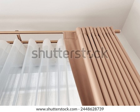 A close-up of a pair of curtains on a window made of a brown and white striped fabric. They are hanging on a curtain rod with maple color that is attached to the top of the window frame.