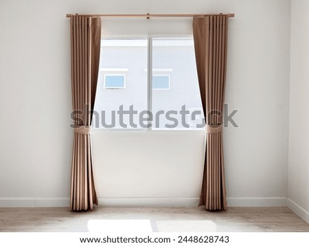 A close-up of a pair of curtains on a window made of a brown and white striped fabric. They are hanging on a curtain rod with maple color that is attached to the top of the window frame.