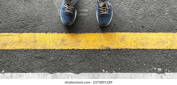 Close-up of a pair of footwear standing behind a yellow line while waiting for a train to arrive