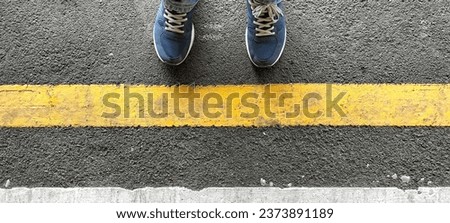 Close-up of a pair of footwear standing behind a yellow line while waiting for a train to arrive