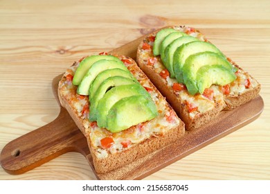 Closeup a pair of homemade grilled cheese toasts topped with avocado and tomato on a breadboard