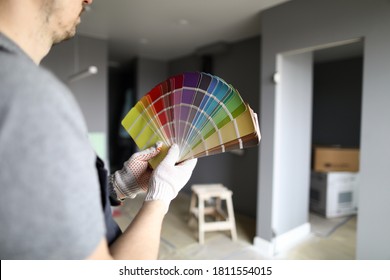Close-up of palettes samples in hands of handyman. Decorating and designing interior, repainting walls with bright colors. Choice of material, selection of tints